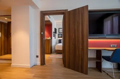 a room with a desk with a tv and a bedroom at Hampton By Hilton Sakarya in Sakarya