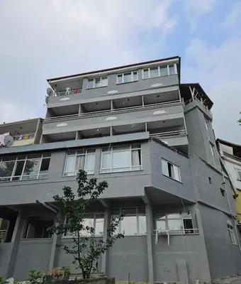 a tall gray building with windows and a tree at Çiğdem Motel Pansiyon & PUB in Termal