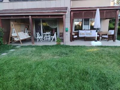a patio with a table and chairs and an umbrella at Garden Floor Flat in a Beachfront Complex with a Pool in Gümüşyaka