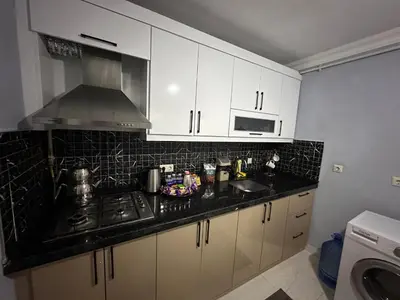 a kitchen with white cabinets and a black counter top at ALTAY Airport SUİT in Tayakadın