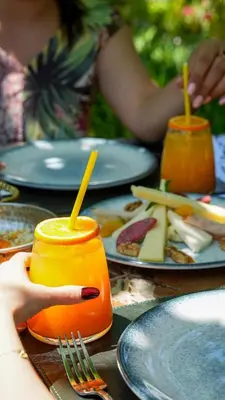a table with plates of food and a person holding a drink at Navy Inn & Bungalows in Arnavutköy