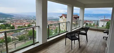 a balcony with two chairs and a view of a city at Luxury villa with sea and forest view in Döngel