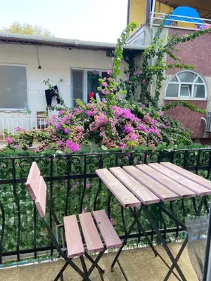 a wooden table and a chair next to a fence with flowers at Büyükada Çarşı Pansiyon in Adalar