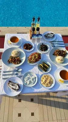 a table with plates of food on a table next to a pool at Grand Şakar Otel in Marmara