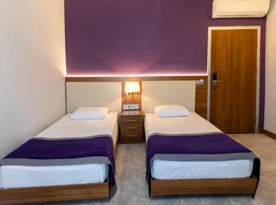 two beds in a hotel room with a purple wall at Business Palas Otel in Kocaeli