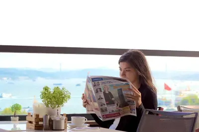 a woman sitting at a table reading a newspaper at Glamour Hotel Istanbul Sirkeci in Istanbul
