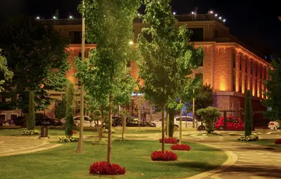 a park with trees and red flowers in front of a building at Antea Palace Hotel & Spa in Istanbul