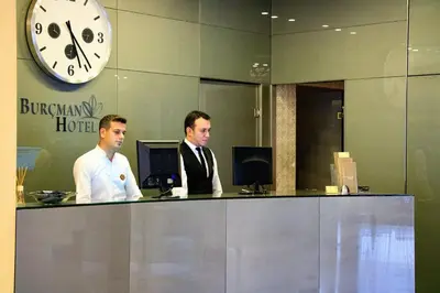 two men sitting at a desk in an office with a clock at Burcman Hotel in Bursa