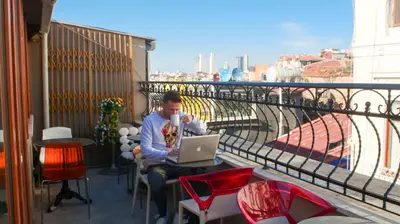 a man sitting at a table with a laptop on a balcony at Stay Inn Taksim Hostel in Istanbul