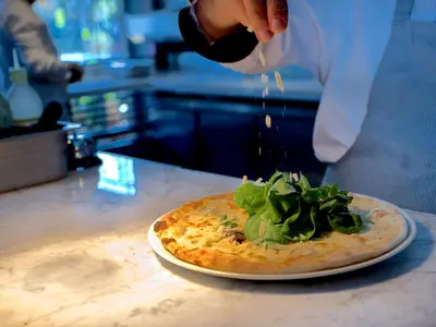 a person is sprinkling sauce on a pizza on a counter at Zimmer Bosphorus Hotel in Istanbul