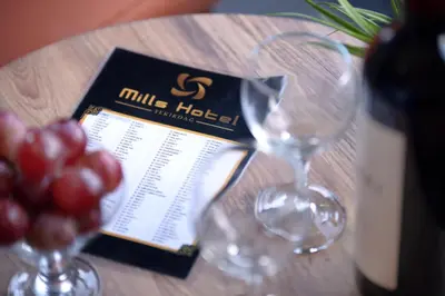 two wine glasses on a table with wine bottles and grapes at MİLLS HOTEL in Tekirdag